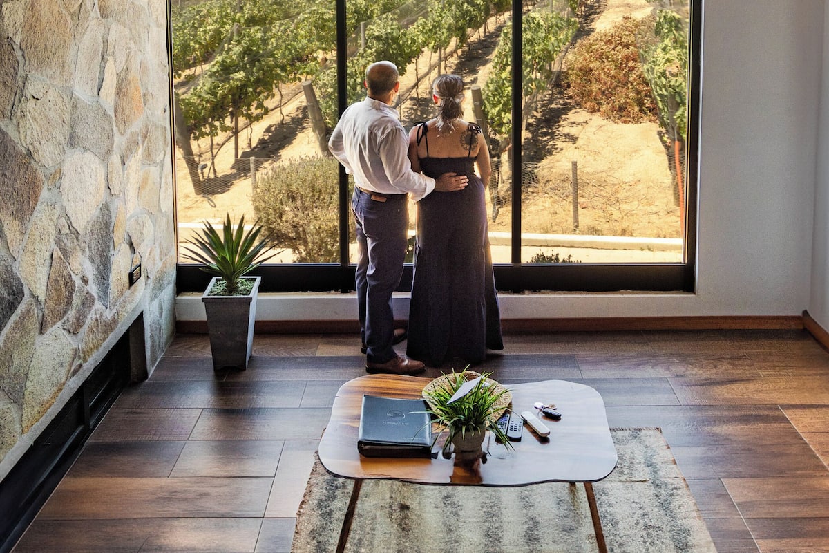 A room with a large window, stone wall, wooden beams, and a rustic rug.