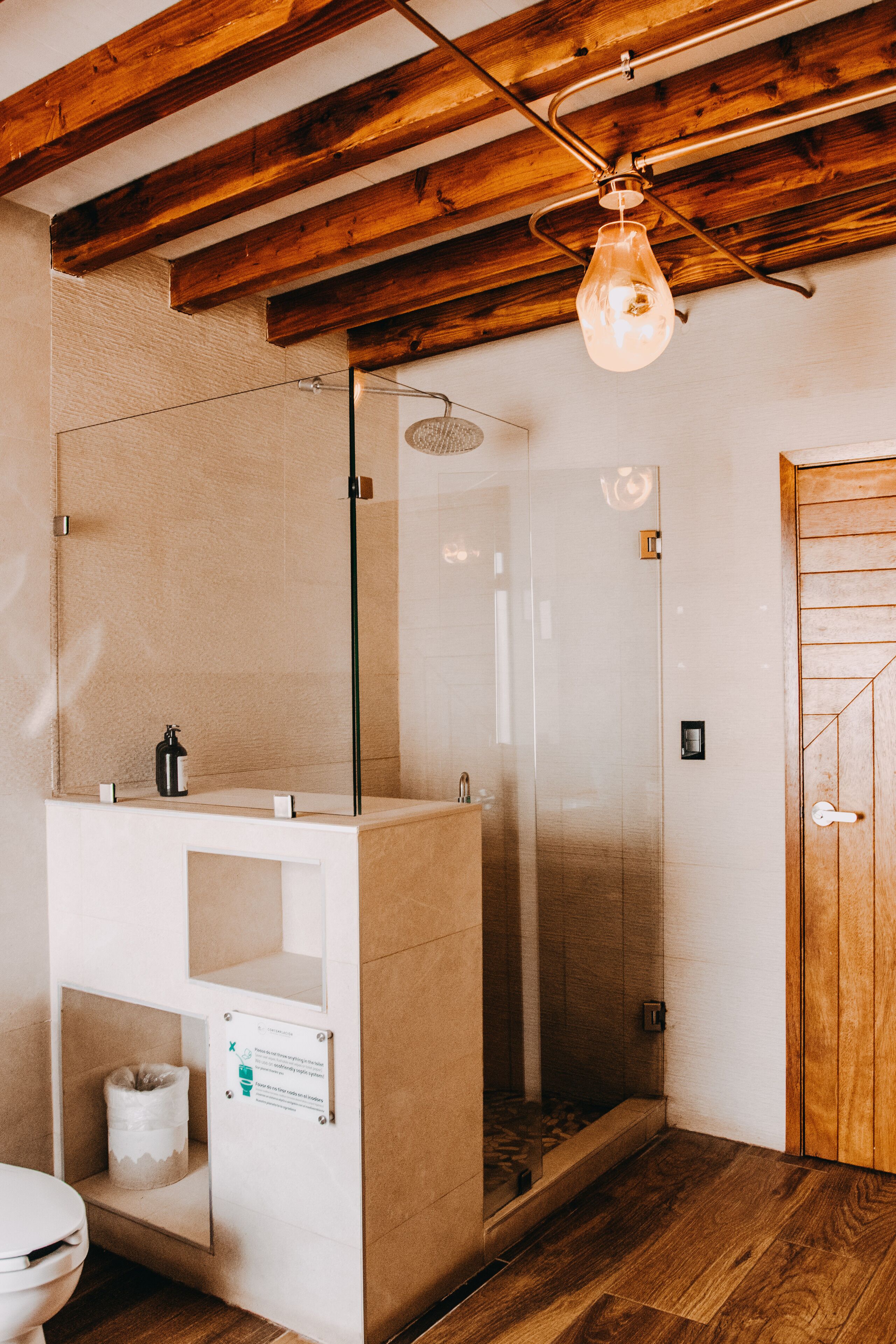A bathroom with a glass shower, wooden ceiling beams, a white sink, and a wooden door.
