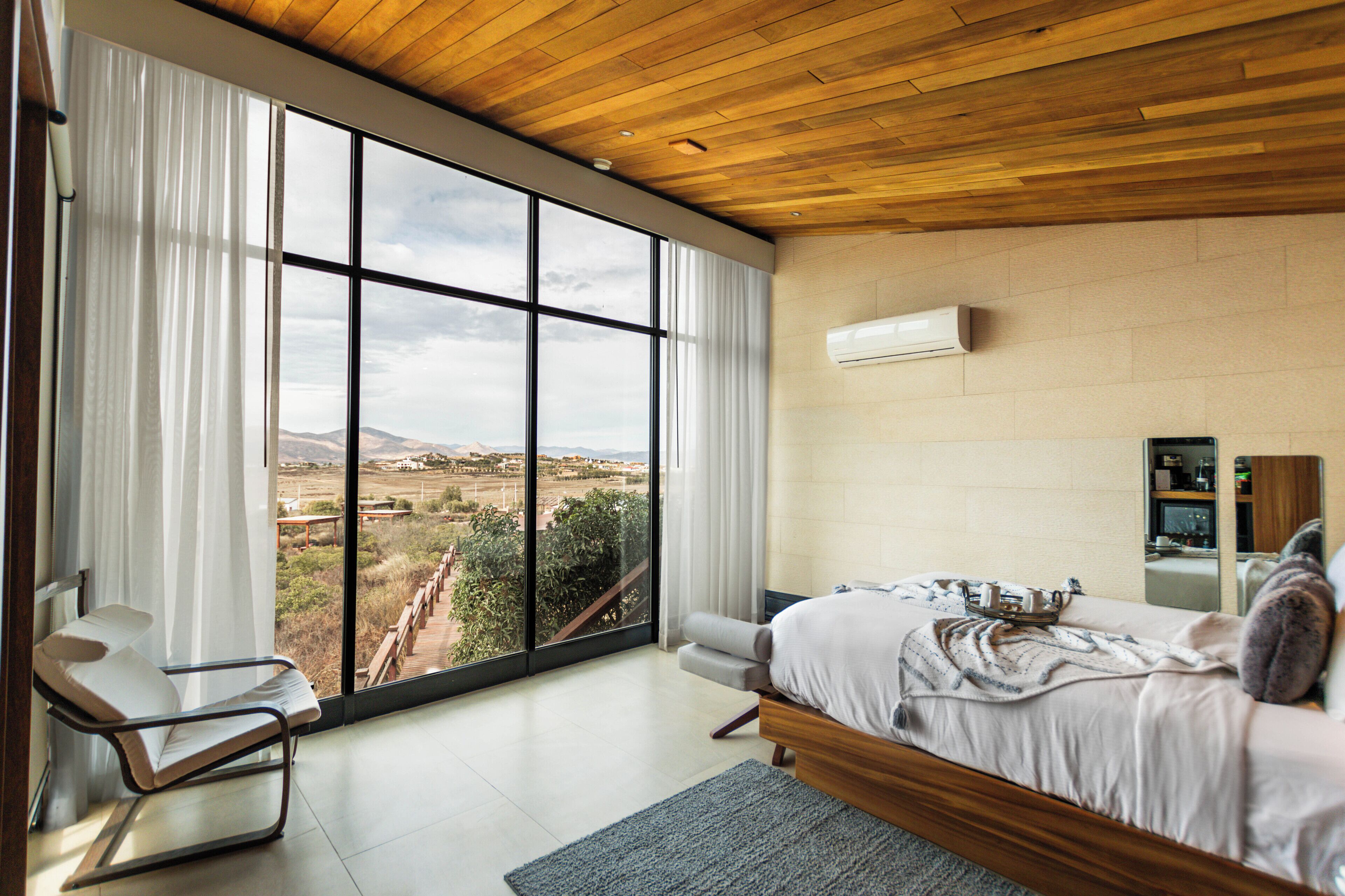 A bedroom with a large window, a bed, a chair, and a wooden ceiling.