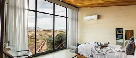 A bedroom with a large window, a bed, a chair, and a wooden ceiling.