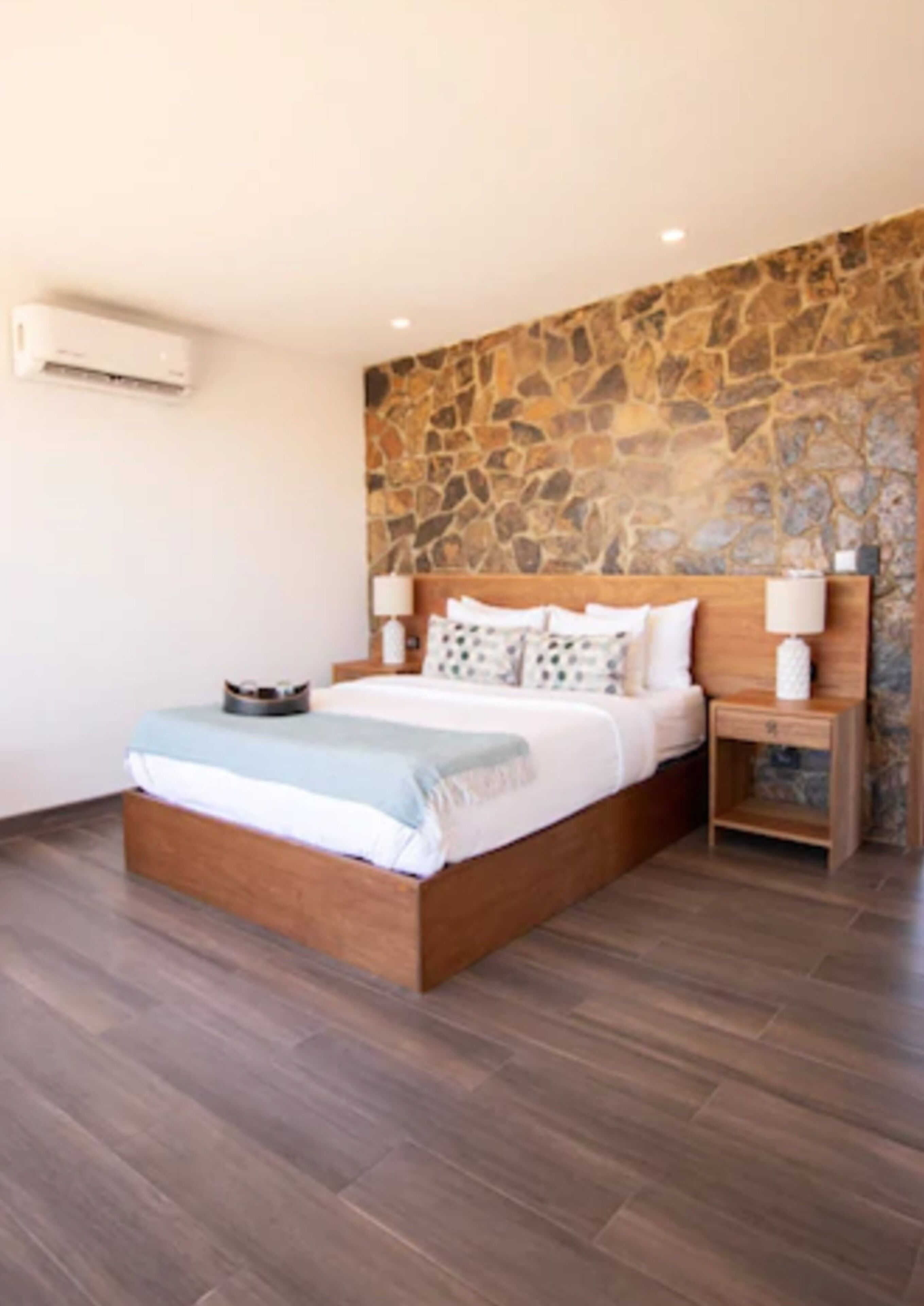 A bedroom with a stone accent wall, a wooden bed frame, and a nightstand with a lamp.