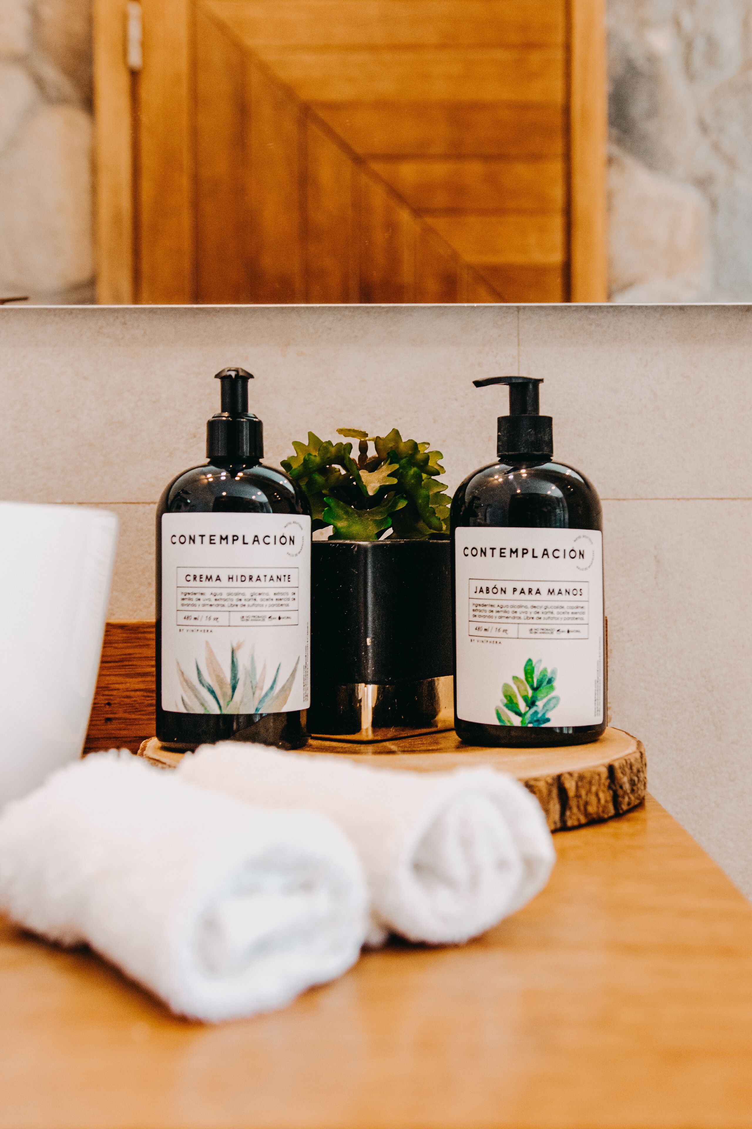 Dos botellas de productos para el cuidado de la piel 'Contemplacion' sobre una superficie de madera, junto a una toalla blanca enrollada.