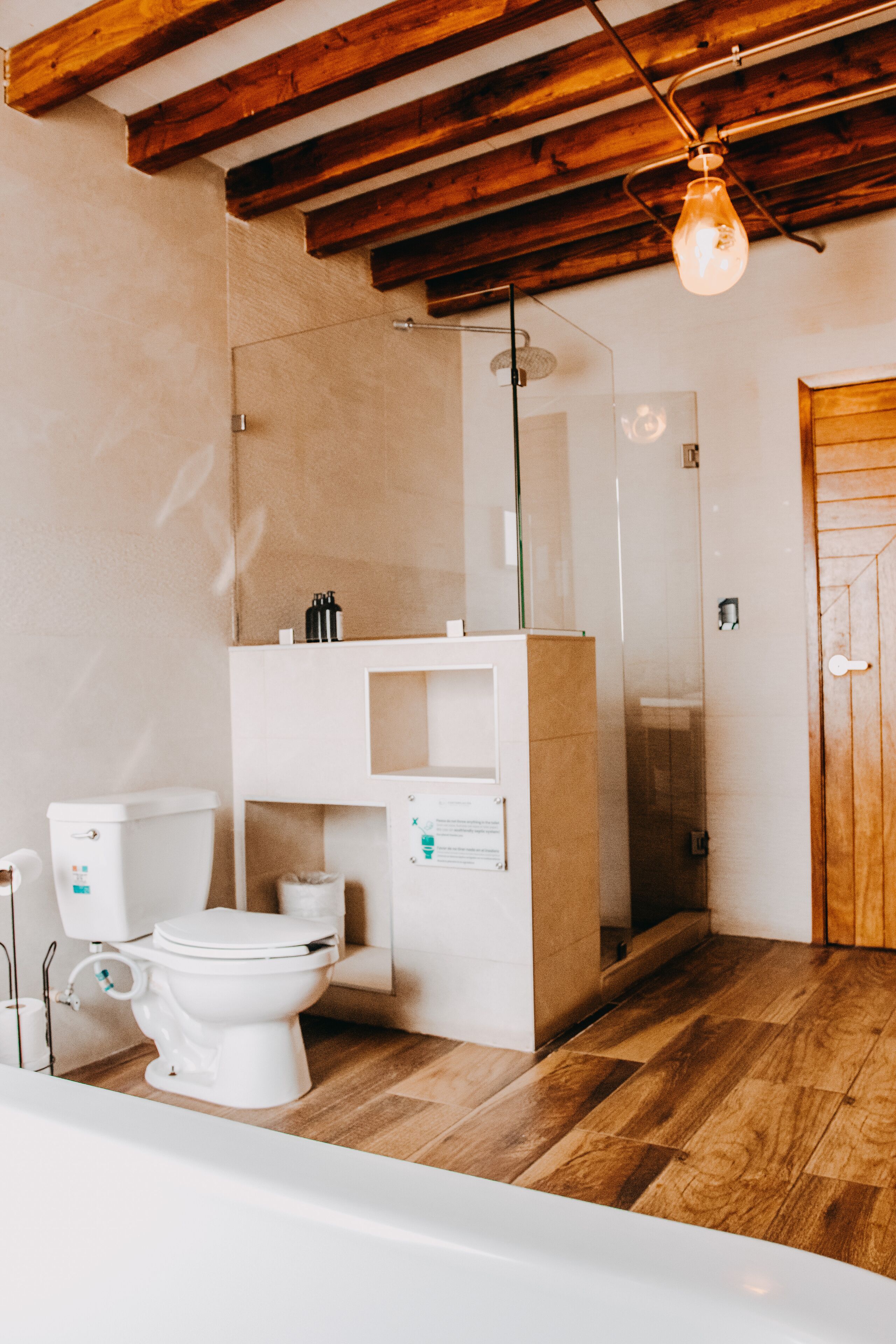 Ein modernes Badezimmer mit Holzboden, Toilette in Weiß, Duschkabine aus Glas und Holztür.