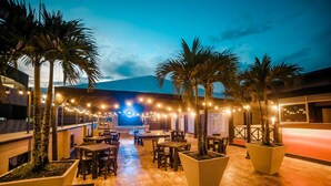 An outdoor patio with tables and chairs, palm trees, and string lights. - Tik by Bernalo Hotels (Medellín)