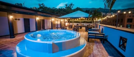 A circular hot tub with a surrounding patio area, outdoor seating, and string lights.