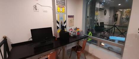 A room with a black desk, two chairs, an air conditioner, and a window with a view of the outside.