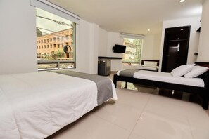 A hotel room with two beds, a TV, a desk, and a window with a view of buildings. - Tik by Bernalo Hotels (Medellín)