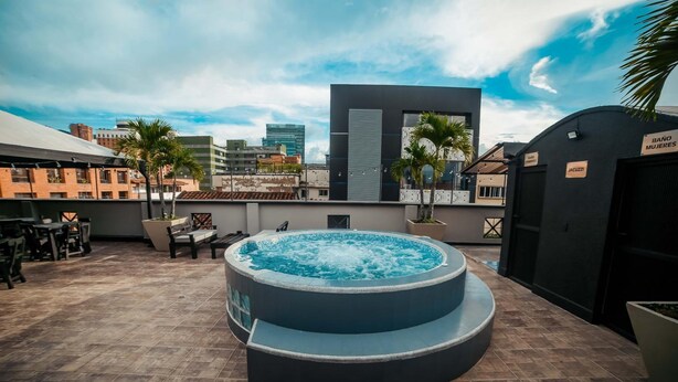 A rooftop pool area with a hot tub, seating, and palm trees. - Tik by Bernalo Hotels (Medellín)