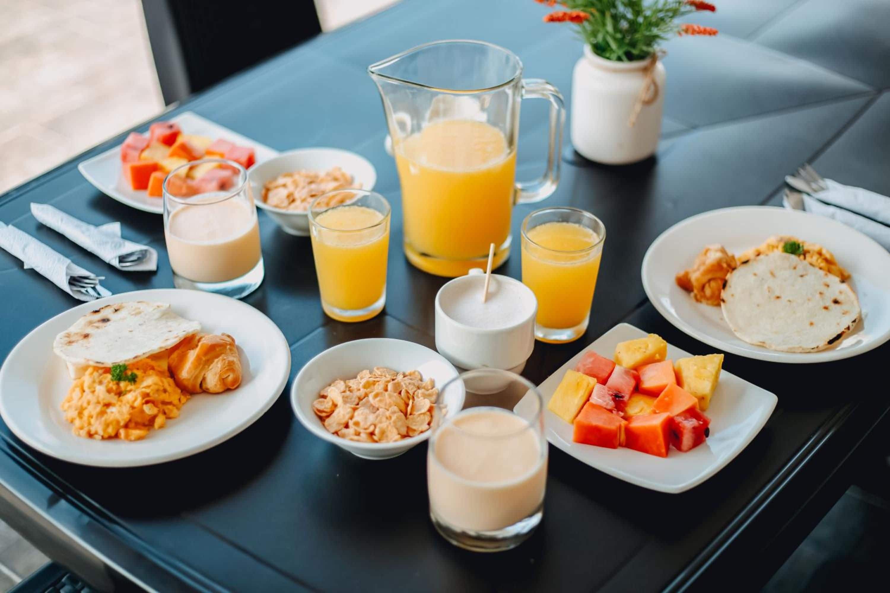 Una mesa de desayuno con platos de comida, vasos de jugo de naranja y una jarrón de jugo de naranja.