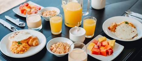 Una mesa de desayuno con platos de comida, vasos de jugo de naranja y una jarrón de jugo de naranja.