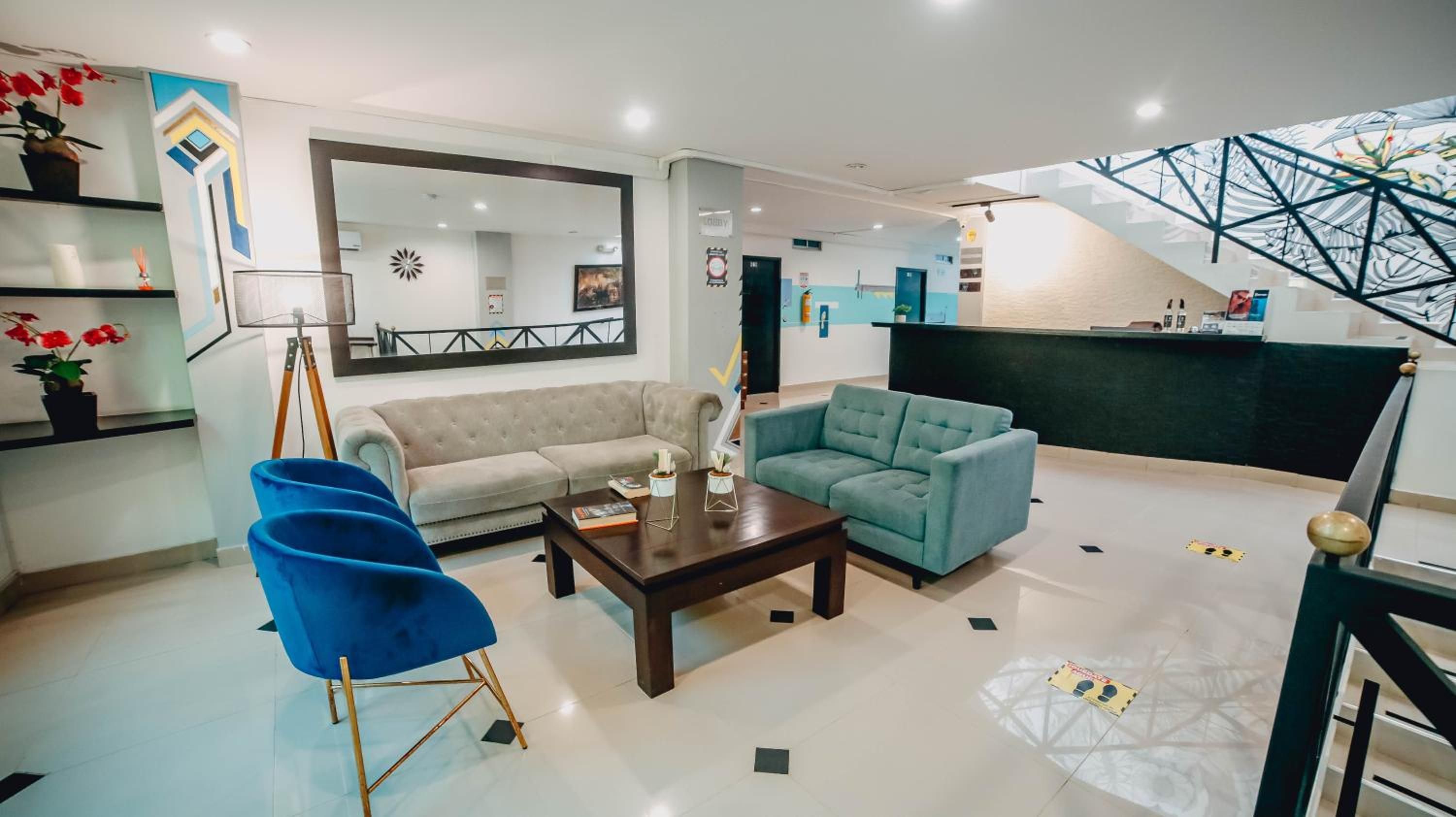 A modern lobby with a sofa, armchair, and coffee table, a reception desk, and a staircase with a geometric design.