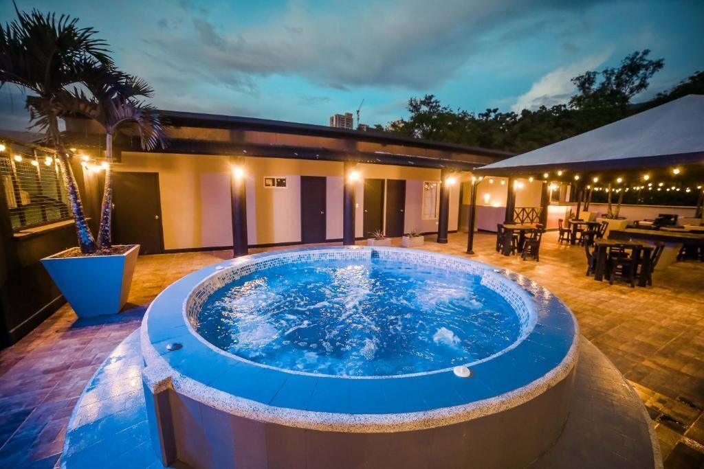 A hot tub with a tiled deck, surrounded by outdoor seating and string lights.