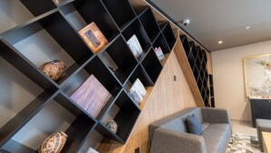 A modern living area with a grey sofa, a black shelving unit with decorative items, and a patterned rug. - Hotel Highland Chihuahua (Chihuahua)
