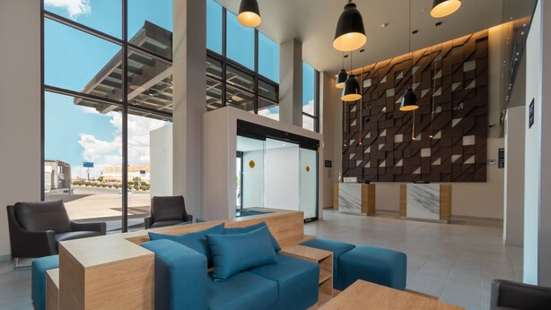 A modern reception area with a blue sofa, wooden reception desk, and a geometric wall design. - Hotel Highland Chihuahua (Chihuahua)
