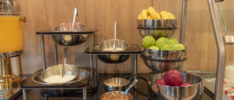 Una mesa de buffet con diversos alimentos, incluyendo frutas, cereales y un tazón de sopa.