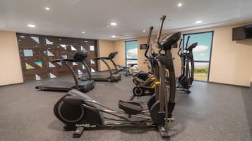 Un gimnasio con diversas máquinas de cardio, un ventanal con vistas y un televisor de pantalla plana montado en la pared.