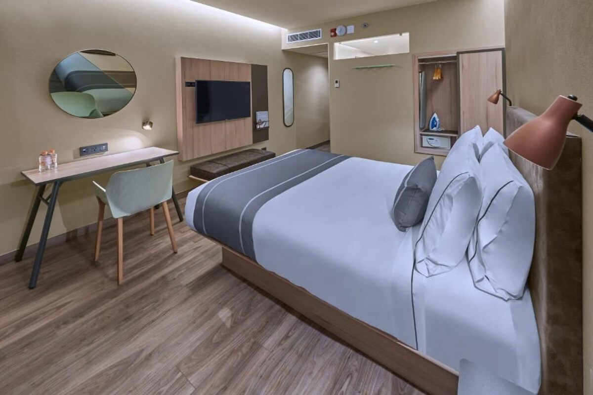 A modern hotel room with a bed, desk, chair, and a television.