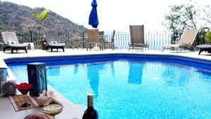 A pool area with lounge chairs, a bottle of wine, and decorative items. - DREAM BAY AND BEACH VIEWS FROM CONDO B3 AT VILLAS ALTAS MISMALOYA (Mismaloya)