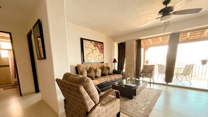A living room with a sofa, armchair, and coffee table. There is a ceiling fan, a framed picture on the wall, and a view of the outside through a glass door. - DREAM BAY AND BEACH VIEWS FROM CONDO B3 AT VILLAS ALTAS MISMALOYA (Mismaloya)