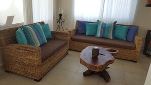 Un salon avec deux canapés en osier, chacun agrémenté de coussins à rayures, et une table basse en bois.