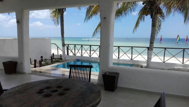 Un espace extérieur abrité comprenant une piscine, une table et une vue sur la plage et l’océan.