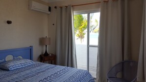Une chambre à coucher avec un lit, une table de chevet, une lampe, une chaise et une vue sur la plage par une fenêtre.