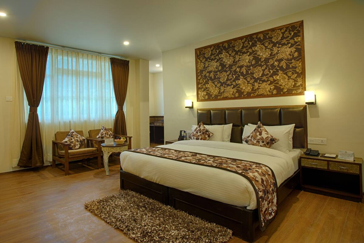 A hotel room with a large bed, a seating area with chairs, a small table, and a decorative wall piece.