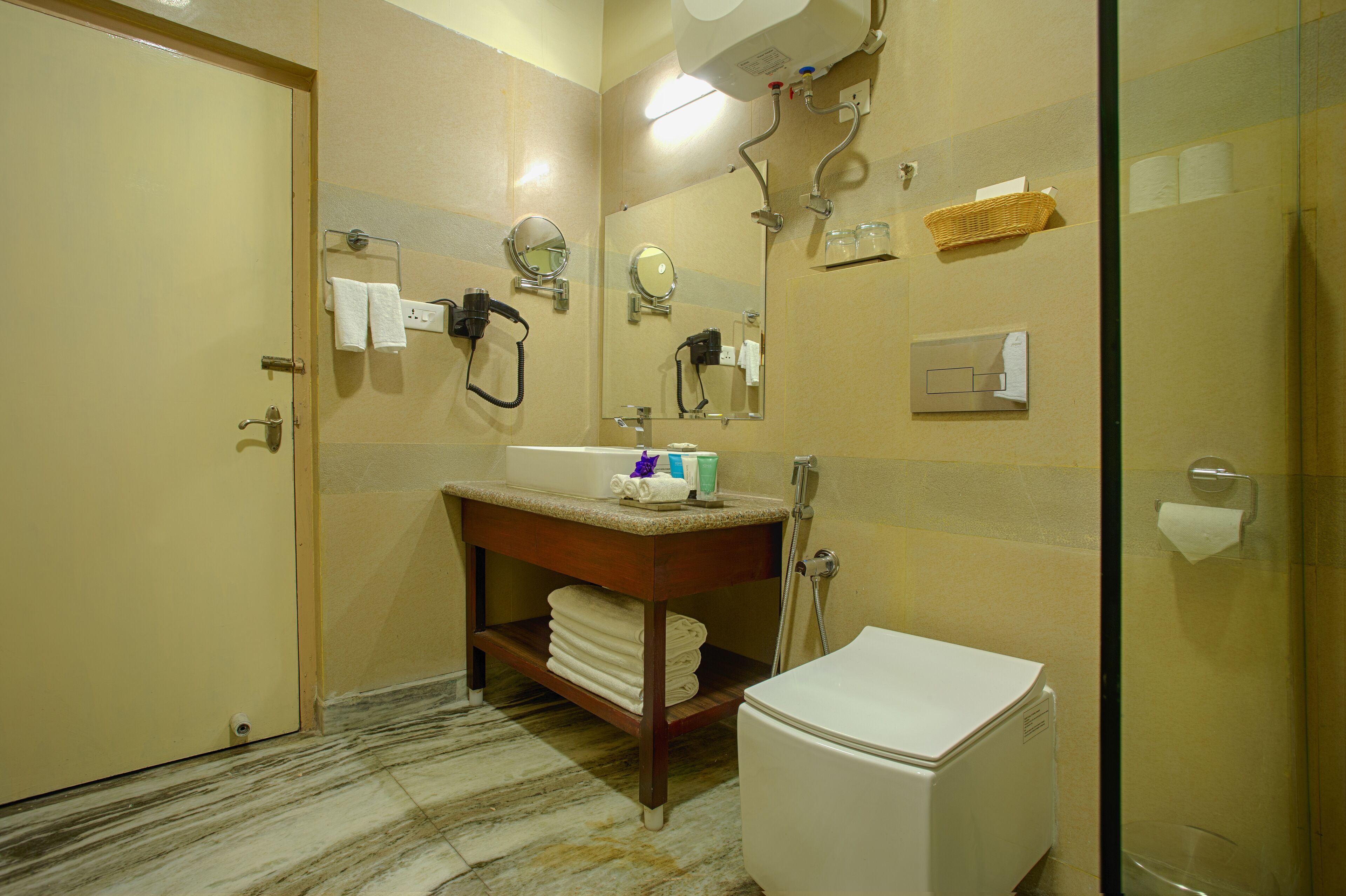 A bathroom with a toilet, sink, and mirror. There is a towel rack with towels, a shower, and a glass-enclosed shower stall.