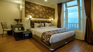 Habitación de hotel con una cama grande, un escritorio con silla, una mesita de noche y vista al mar a través de una ventana.