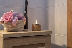 A wooden bedside table with a woven candle holder and a basket containing pink flowers.
