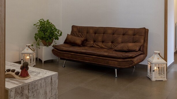 Een gezellige woonkamer met een bruine leren bank, een witte bijzettafel met een plant en een decoratieve lantaarn.