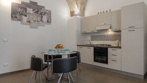 Een moderne keuken met witte kastjes, een eettafel met stoelen en een decoratief wandobject.