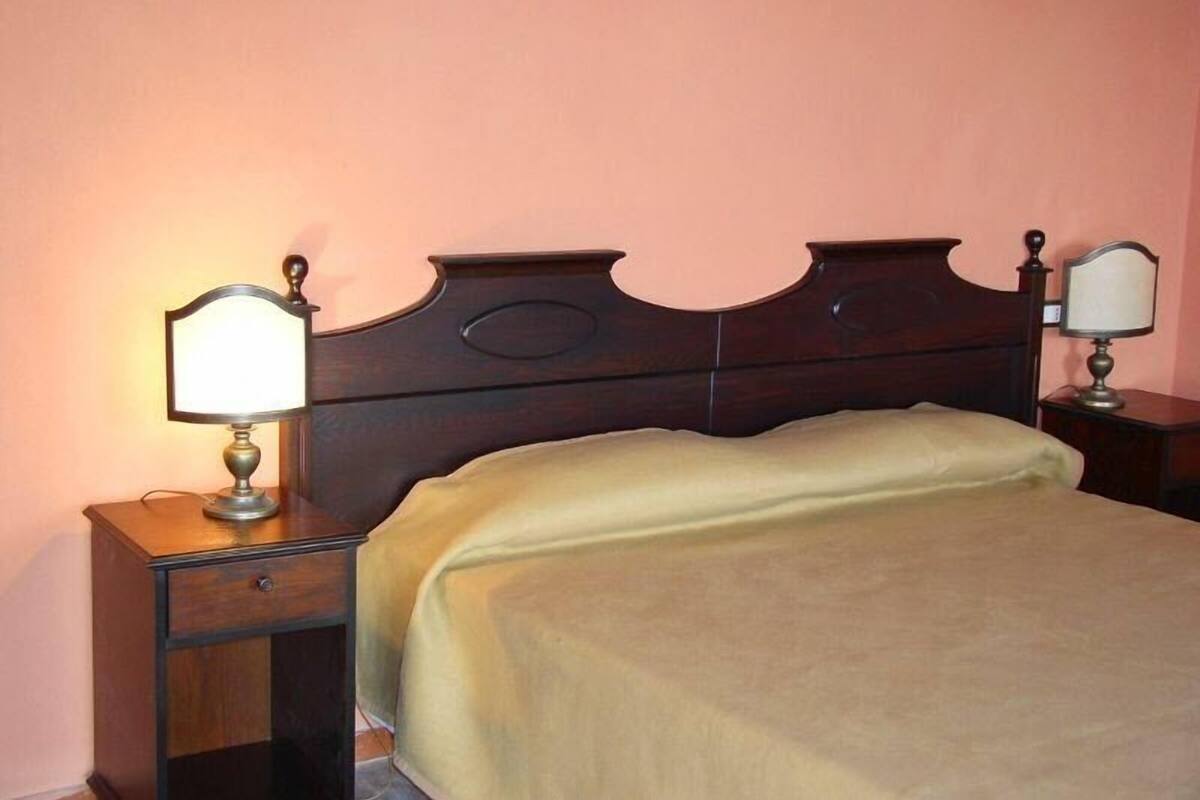 Un dormitorio con cabecera de madera, una cama con manta color beige y dos mesitas de noche con lámparas.