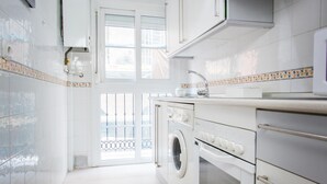 A modern kitchen with white cabinets, a built-in oven, a microwave, and a washing machine.