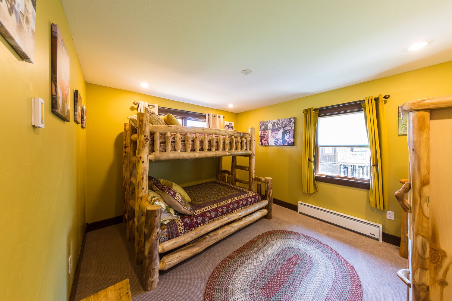 A room with a rustic wooden bunk bed, a patterned rug, and a window with curtains.