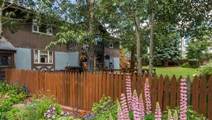 Il s’agit d’une propriété résidentielle dotée d’une clôture en bois, d’un jardin agrémenté de diverses fleurs et d’une maison à l’extérieur bleue, avec une terrasse en bois.