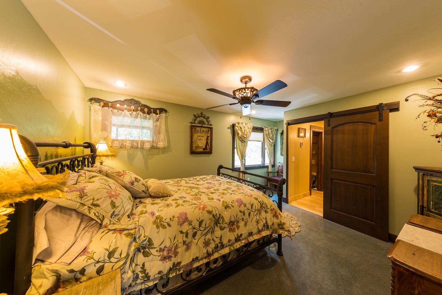 A bedroom with a bed, a ceiling fan, a window with curtains, and a door leading to another room.