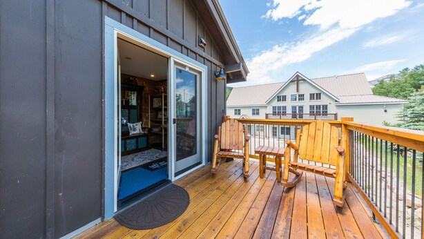 Une terrasse en bois avec une porte-fenêtre coulissante donnant sur une pièce où se trouvent un tapis bleu et un petit tapis.