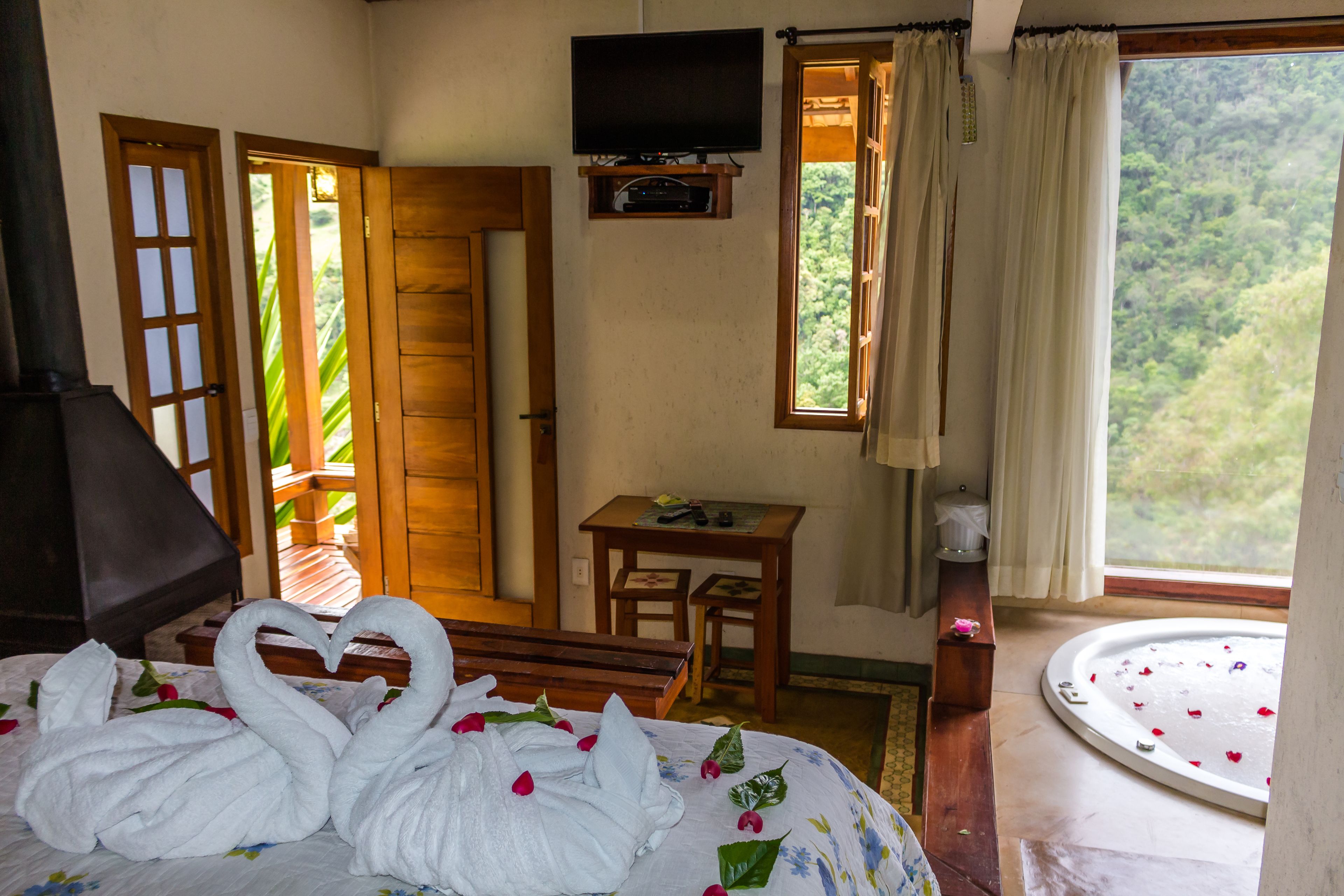 Una habitación con cama, televisión, ventana con cortinas, un banco de madera y una pequeña mesa.