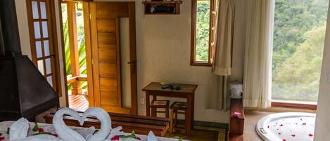 Una habitación con cama, televisión, ventana con cortinas, un banco de madera y una pequeña mesa.