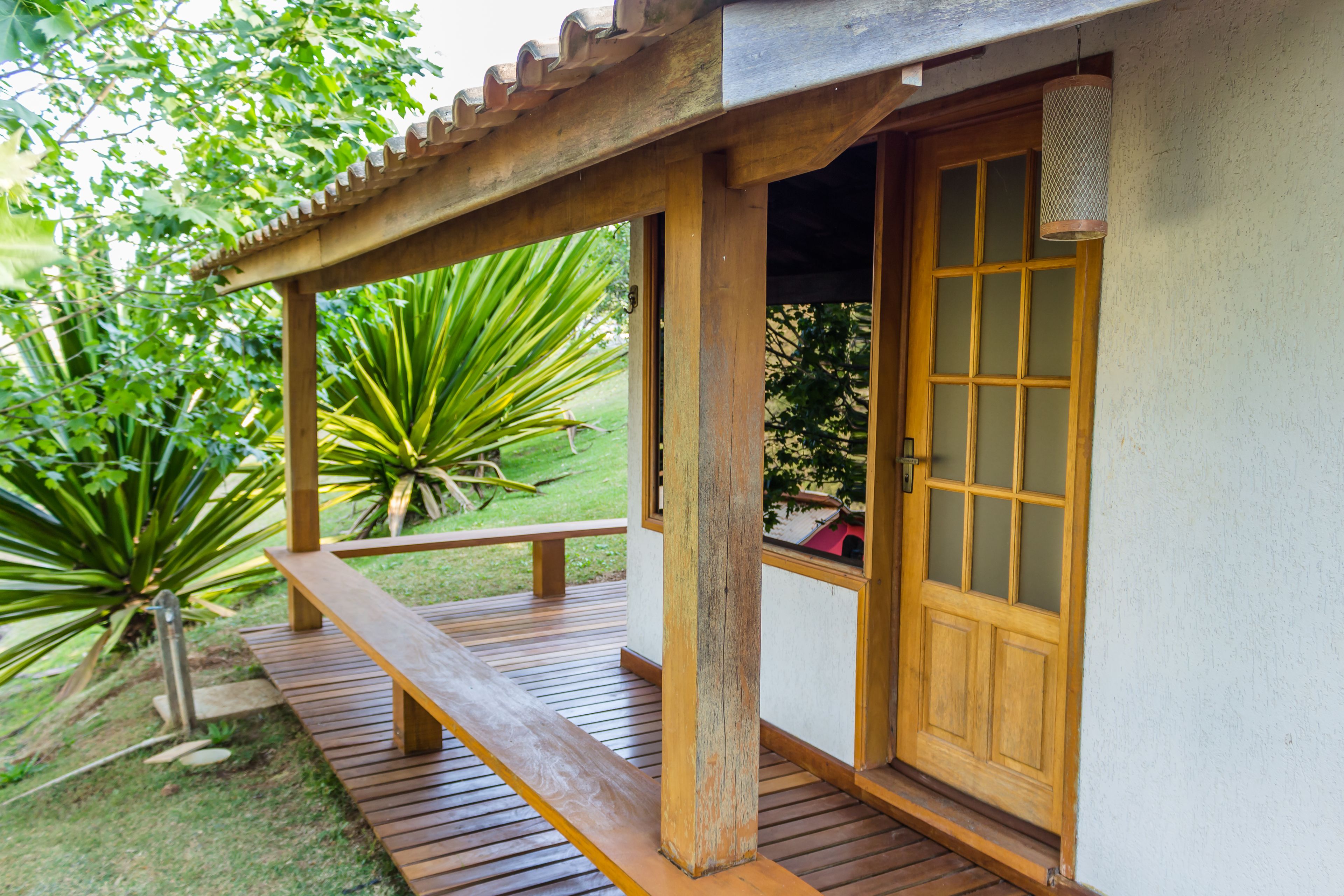 Um deck de madeira com um banco, uma porta com painéis de vidro e uma pérgula.