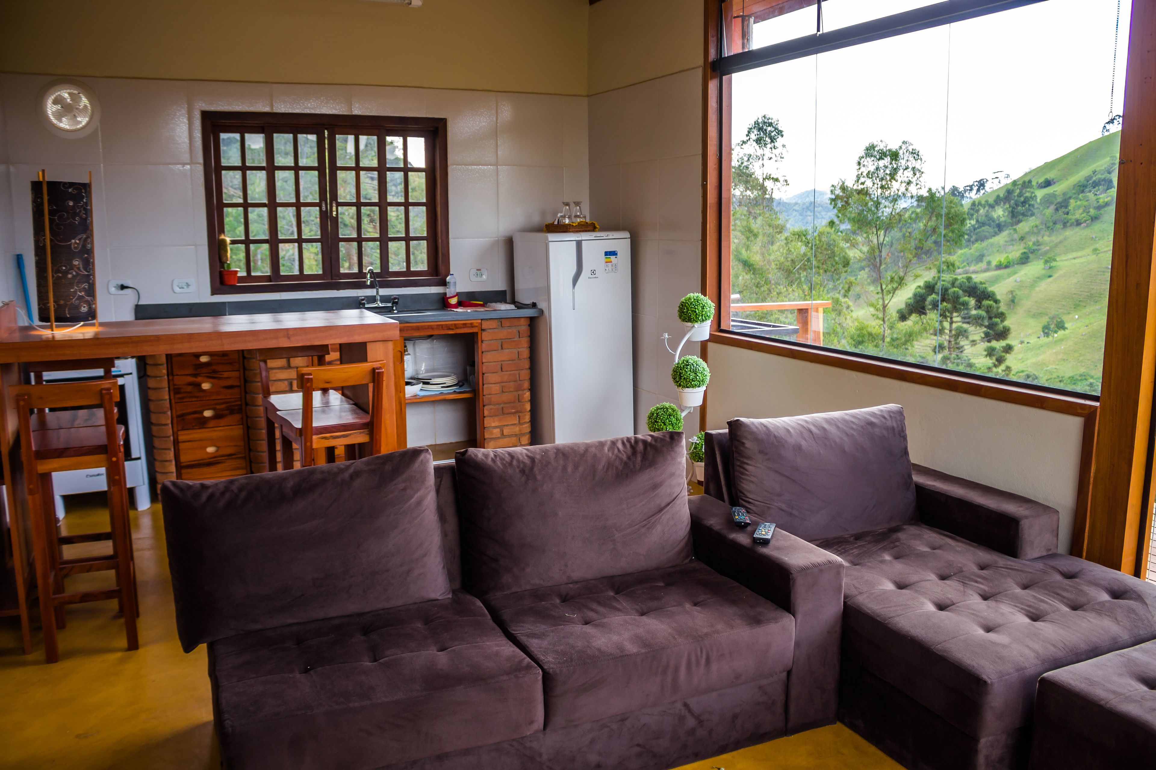 A cozy living area with a sofa and armchairs, a kitchen with a refrigerator and window, and a view of a green landscape.