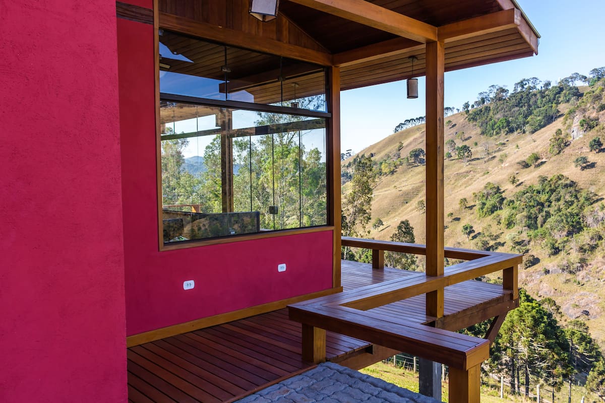 A modern building with a red exterior, large windows, and a wooden deck overlooking a hilly landscape.