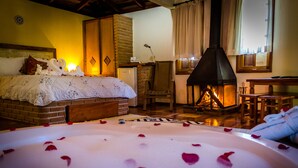 A cozy bedroom with a large bed, a fireplace, and a bathtub with rose petals. - Pousada Espelho DÁgua (Gonçalves)