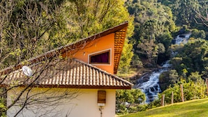 A house with a tiled roof, a small window, and a view of a waterfall in the background. - Pousada Espelho DÁgua (Gonçalves)