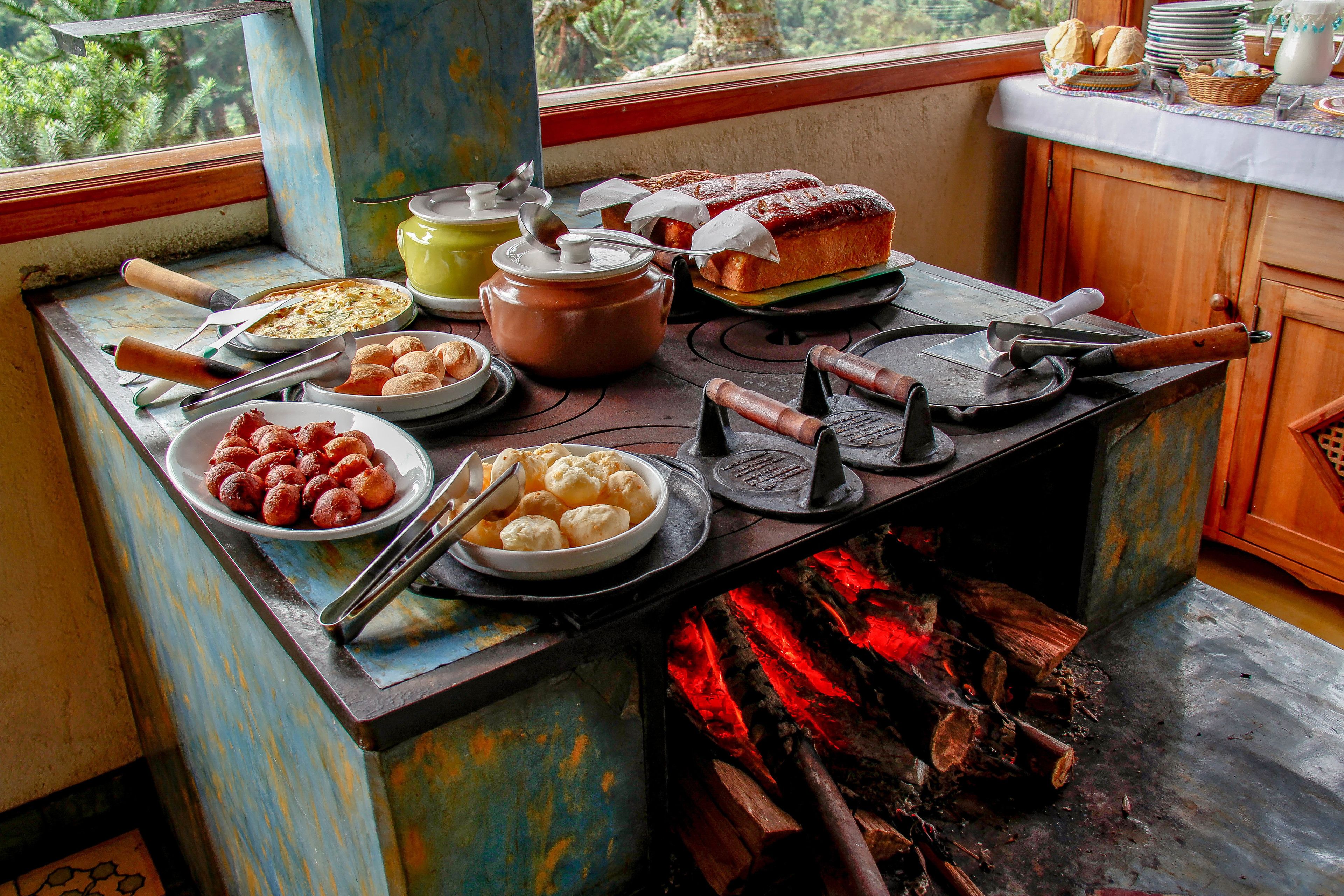 Una cocina rústica con un fogón de leña, distintos utensilios de cocina y alimentos sobre la encimera.
