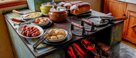 Una cocina rústica con un fogón de leña, distintos utensilios de cocina y alimentos sobre la encimera.