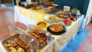 Un bufé con diversas opciones de comida, incluyendo pasteles, frutas y un cartel que indica 'desayuno griego'.