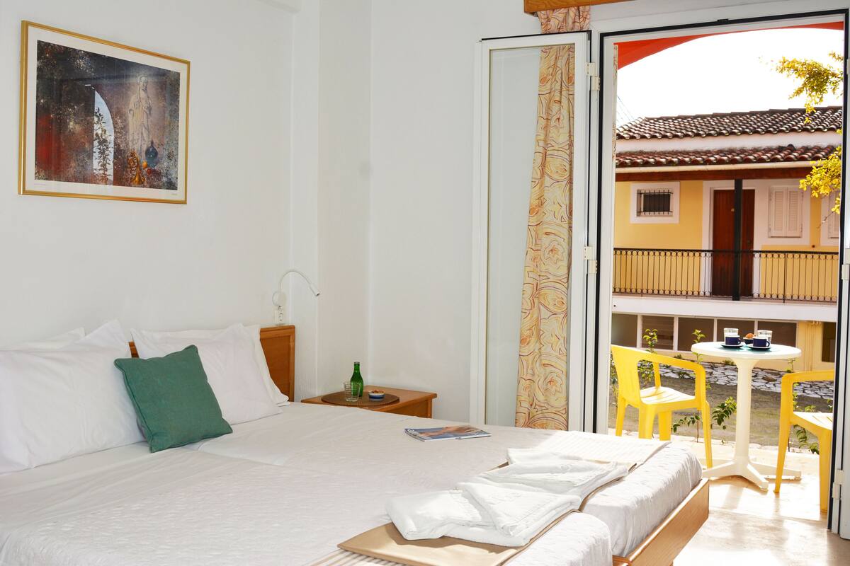 Habitación de hotel con cama, mesita de noche, ventana con vista al balcón exterior y un cuadro en la pared.