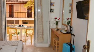 A hotel room with a bed, a desk with a chair, a small table with a chair, a window, and a balcony with a table and chairs.